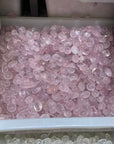 A large white plastic storage bin filled with many small, smooth, translucent pink stones or beads, photographed from above. A second drawer or bin at the bottom edge shows pale clear stones.