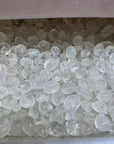 Clear, translucent pebble-shaped decorative stones or beads filling a container, with a soft pinkish-white translucent lid or liner visible at the top.