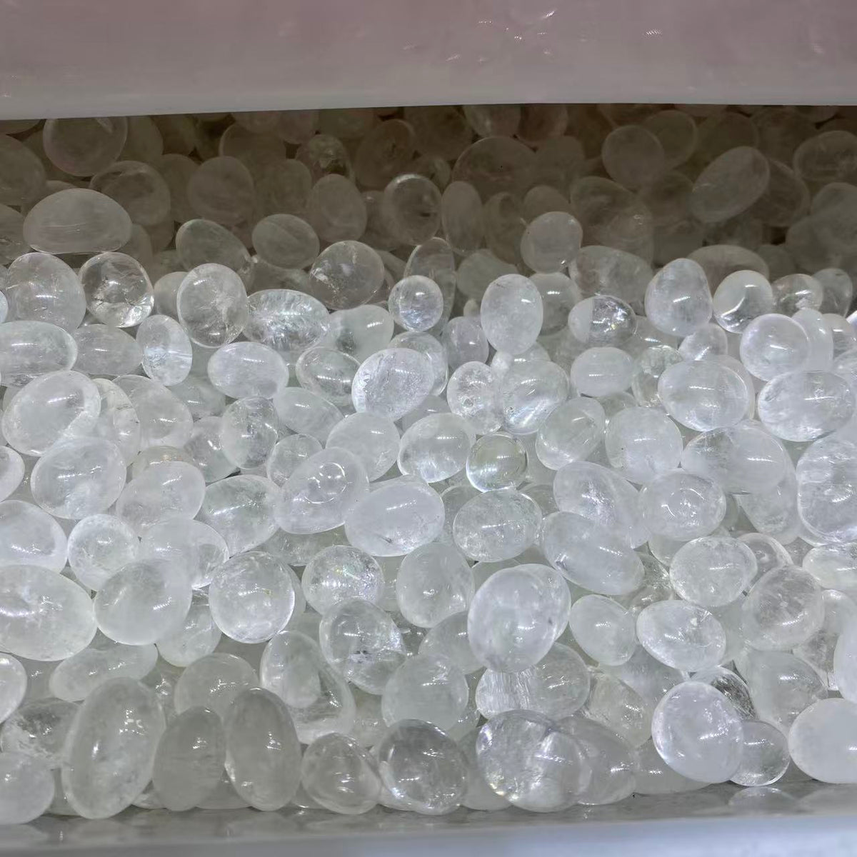 Clear, translucent pebble-shaped decorative stones or beads filling a container, with a soft pinkish-white translucent lid or liner visible at the top.