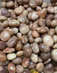 A close-up pile of smooth, polished decorative stones in earthy tones, including beige, brown, pink, and cream, filling the frame.